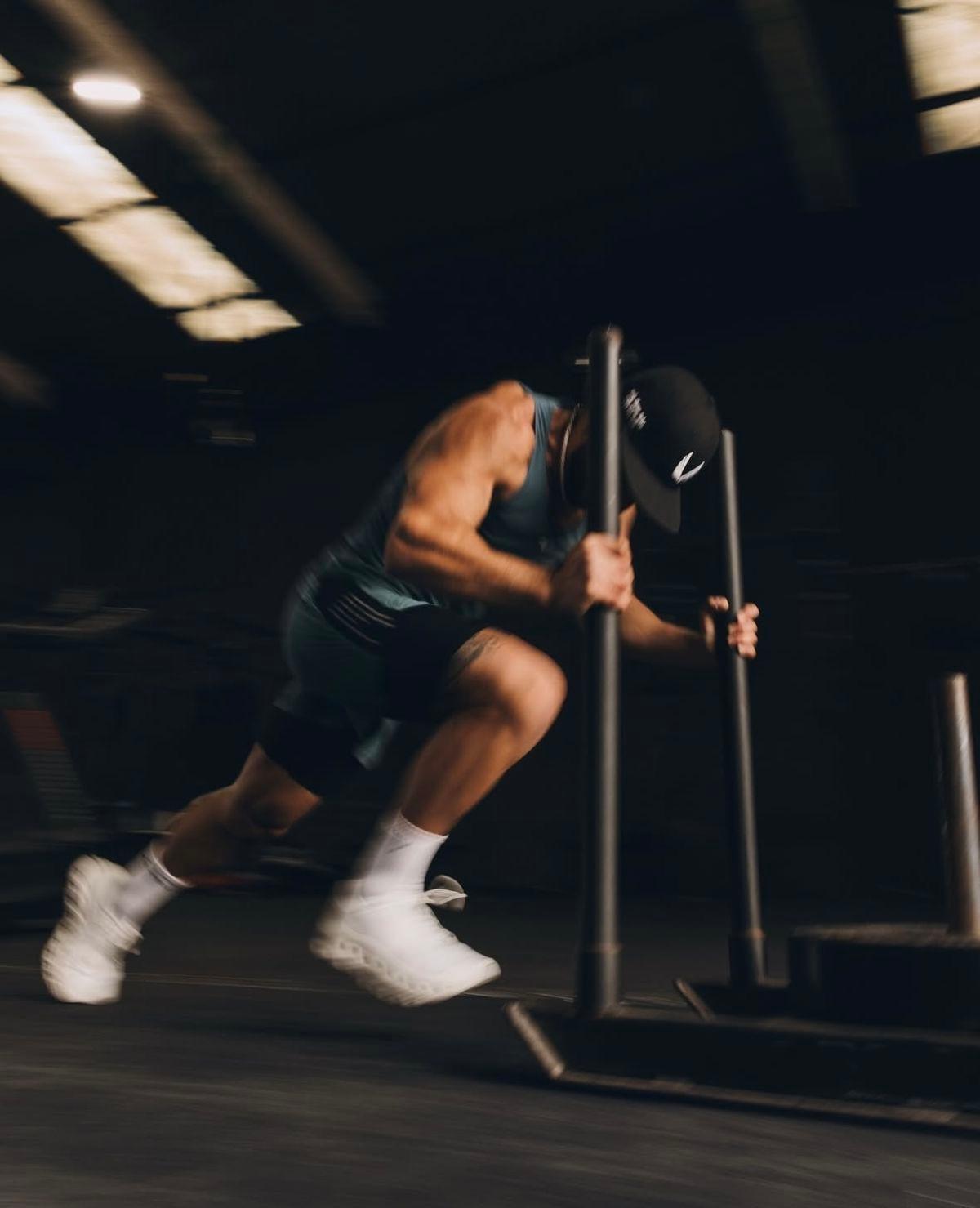 A lifter driving a loaded sled forward, caught mid-stride in motion blur